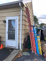 Two ladders stacked against exterior wall of a building, one yellow and blue, one red, showing size and color details.