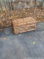 Photo showing the lobster trap from the front and side on pavement with dry leaves in the background.