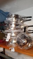 Stack of stainless steel pots and pans wrapped in plastic, showing multiple cookware items with handles and a flat bottom.
