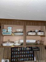Upper cabinet view showing all dishes on two shelves: Pyrex Butterprint set at lower right, CorningWare and Corelle pieces above and to left