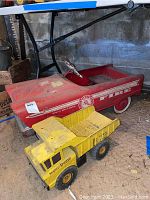 Side view of red metal child's ride-on fire truck with whitewall tires and circular fire department logo, placed near yellow Tonka Mighty Dump truck with visible wear.