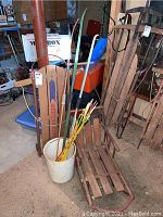 Shows the baby sled, Western Clipper sled, bows, and arrows together in a storage setting