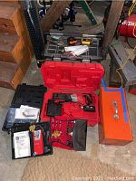 Overview of multiple tool boxes and tool cases, showing red cordless drill and orange metal tool box.