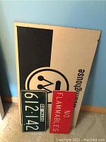 Large Westinghouse sign, No Flammables sign, and 1966 Massachusetts license plate leaning against a wall on carpeted floor