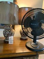 Two brown/black/cream patterned ceramic lamps with round wooden bases and translucent brown lampshades alongside a black Comfort Zone electric fan on a wooden surface.
