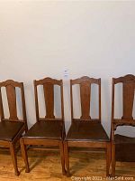 Four matching oak chairs lined up against wall showing full set