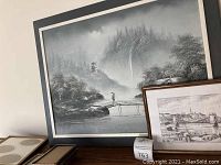 Large black, white and gray oil painting of Japanese waterfall, bridge and pagoda with small framed pen and ink drawing of Budapest bridge in front and some empty frames placed next to them on the floor