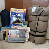 Camping lot contents including tent box, sleeping bags, air beds in boxes, mess kit, and Coleman toaster box.