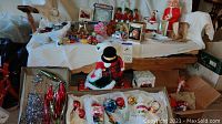 Wide shot showing a variety of vintage Christmas ornaments spread out on a couch and a box of ornaments in the foreground, including tinsel and an angel hair.