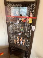 Full view of the tall dark brown corner shelf with geometric lattice wood design and plexiglass door. Several small figurines displayed inside.