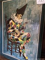 Full view of framed painting depicting a harlequin playing a stringed instrument