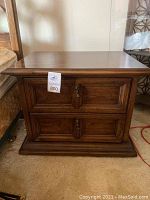 Front view of one of the two dark finish night stands showing two drawers with decorative handles and molding detail.
