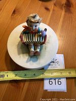 Top view of covered box with boy figurine playing accordion and a bird on the accordion, showing approximately 5 inch diameter.