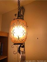 Front view of amber glass hanging light illuminated, showing black metal scrollwork and chain suspension.
