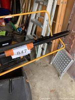 Close-up of black Popular Pro gas mower showing some controls and a number label, with aluminum step stool in background
