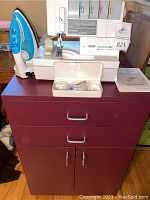 Serger machine and iron on top of purple cabinet with drawers and doors