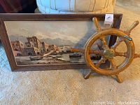Ship’s wheel leaning against framed seaside painting