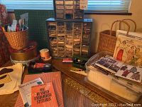 Wide view of the sewing notions and organizing cabinetry on a table surface, including baskets, books, ribbon spools, and pattern booklets.