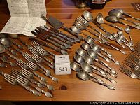 Overview of assorted forks, spoons, knives and servers arranged on wooden table.