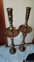 Pair of tall brass candle holders showing full height and design details.