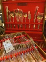 Photo of various flatware items including serving pieces held in a red felt-lined wooden case with slots for each piece.