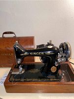 Side view of the Singer sewing machine on wooden base with ornate gold detailing and Singer logo.