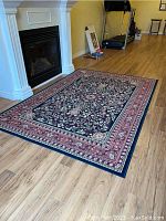 Full view of the rectangular floral patterned area rug on wood floor near fireplace and treadmill.
