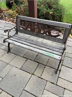 Full view of child's bench showing wood slatted seat, cast iron armrests and legs, and decorative cast iron backrest insert