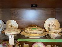 Limoges covered dishes, plates, sugar bowl (missing lid), and sauce boat arranged on wood shelf with floral patterns and gold accents