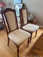 Pair of armless wooden dining chairs with beige patterned upholstery and carved wooden frames.