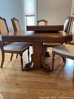 Side view of dining table showing ornate pedestal base and medium-brown wood finish