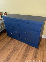 Front view of blue solid wood dresser showing six drawers with different knobs and handles.