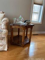 Wooden end table with beveled glass top holding glassware, next to floral couch