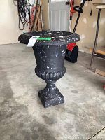 Front view of the black concrete composite flower urn showing paint chipping and overall shape.