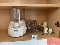 Cuisinart food processor base unit with mixing bowl and blade attachments on wooden shelf.