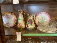 Glass shelf showing floral china plates, pitchers, and glass bowls with price tags