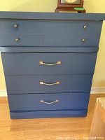 Blue painted high boy dresser with four drawers showing the front view including brass knobs and handles.