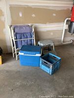 Photo of two folded lawn chairs, blue Rubbermaid cooler, light gray plastic step stool, and blue milk crate against a garage wall