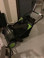 Full view of the Earthwise Sweep It leaf sweeper showing its green and black body with a mesh collection bag attached to the rear and ergonomic handle.