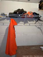 Photo showing orange fleece jacket hanging on a wire rack along with orange caps, gloves, and other clothing items.