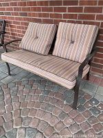 Front view of the brown metal patio love seat with striped cushions, showing seat and back cushions and armrest detail.