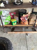Image showing various bags and containers on a metal shelf including polymeric sand, paver sand, gardening fertilizers, and a sealant canister.