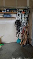 Full view of the corner showing scrap wood stacked beside the wall, hanging ropes and cords, and shelves with containers of screws and other hardware items.