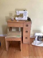 Front view of white Sears Kenmore sewing machine on solid wood desk with three drawers, wooden stool in front.