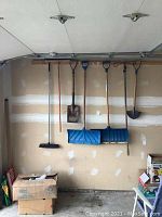 Wide view of all hanging tools including snow shovels, spade, broom, rake, hand brush, and edger