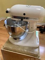 White KitchenAid stand mixer on cardboard box, front-left view showing tilt-head and bowl