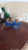 3 inch swivel base vise placed on a workbench showing front and side view with blue metal body and metal jaws