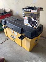 Yellow and black plastic tool box with metal latches and handle, placed under the headphone box