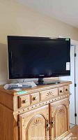 Samsung 31 inch LCD TV on wooden cabinet with remote and manual on top, screen off.