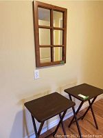 Two brown painted wood folding tables and window pane mirror on wall